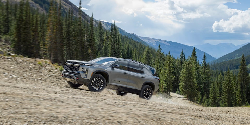 2024 Chevrolet Traverse driving uphill on a tree-lined mountain road.