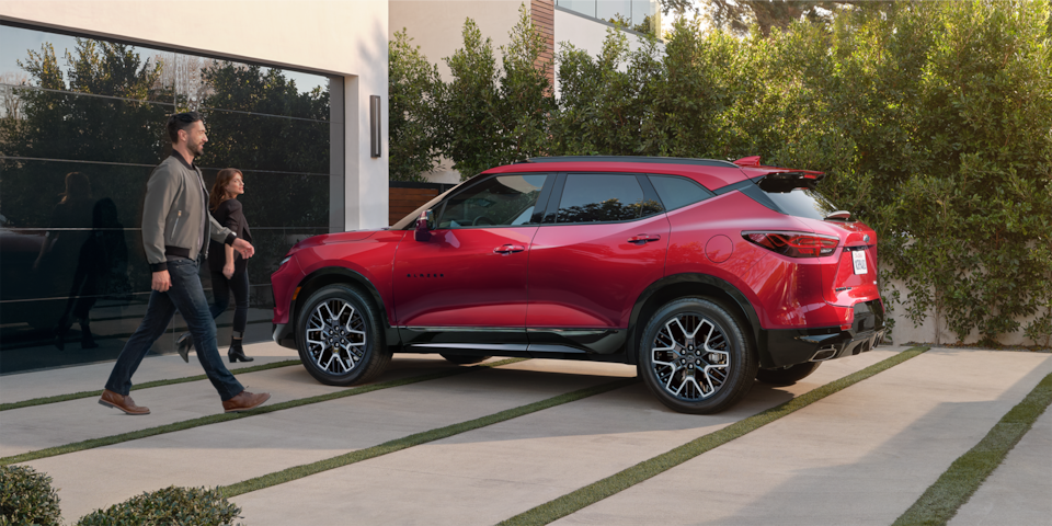 Two people walking past the 2025 Chevrolet Blazer parked outside a modern home.