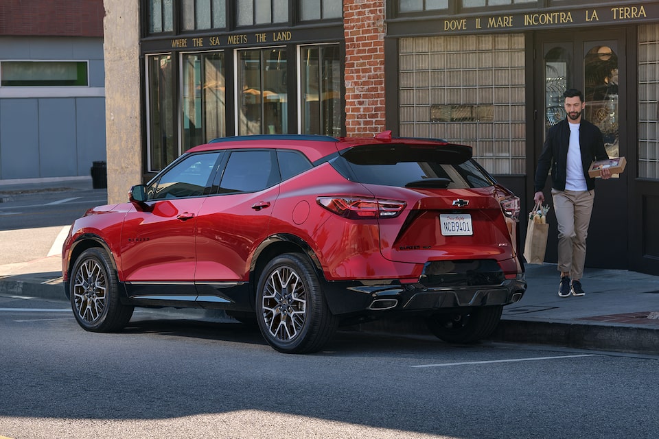 Rear-side view of the 2025 Chevrolet Blazer parked outside a building as a person passes by.