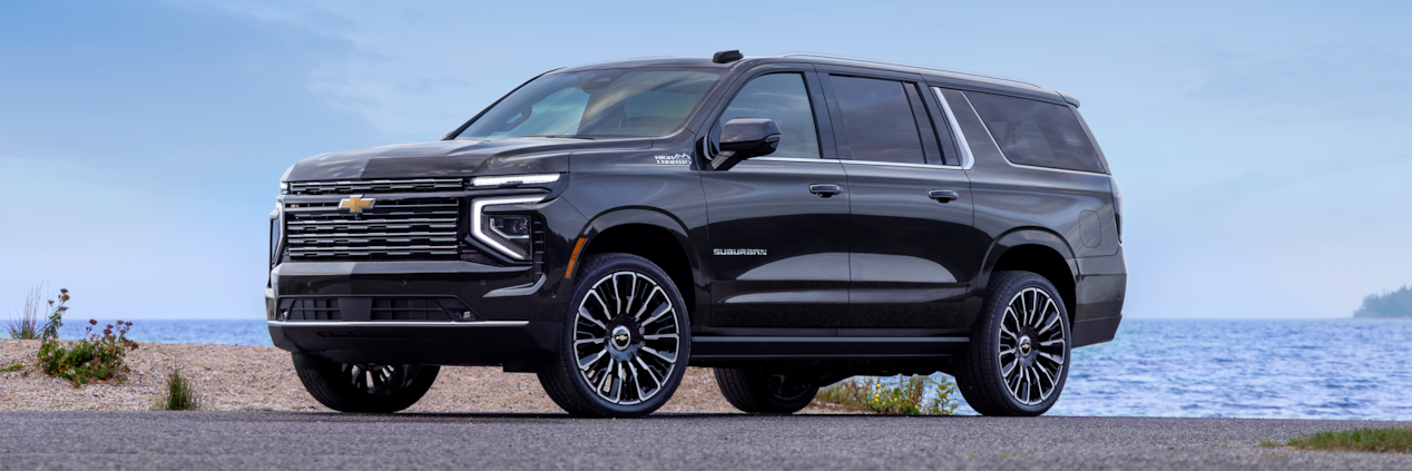 Front-side view of the 2025 Chevrolet Suburban SUV parked by the lake.