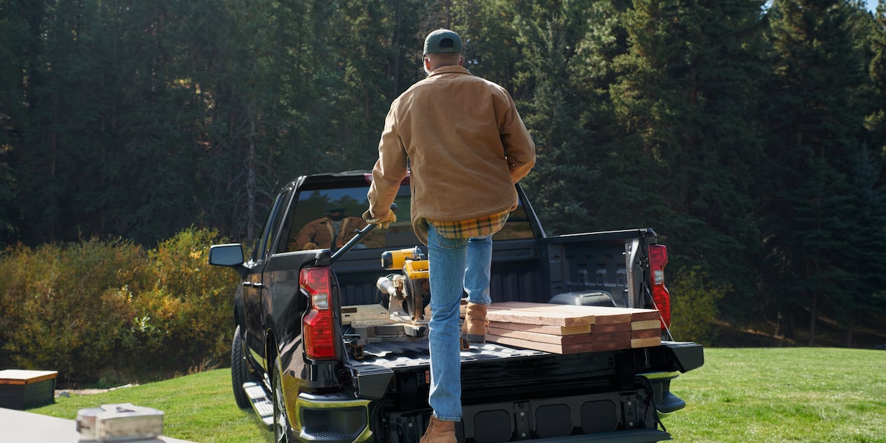 A person putting wood and other equipment on the trunk of a 2025 Chevrolet Silverado LD.