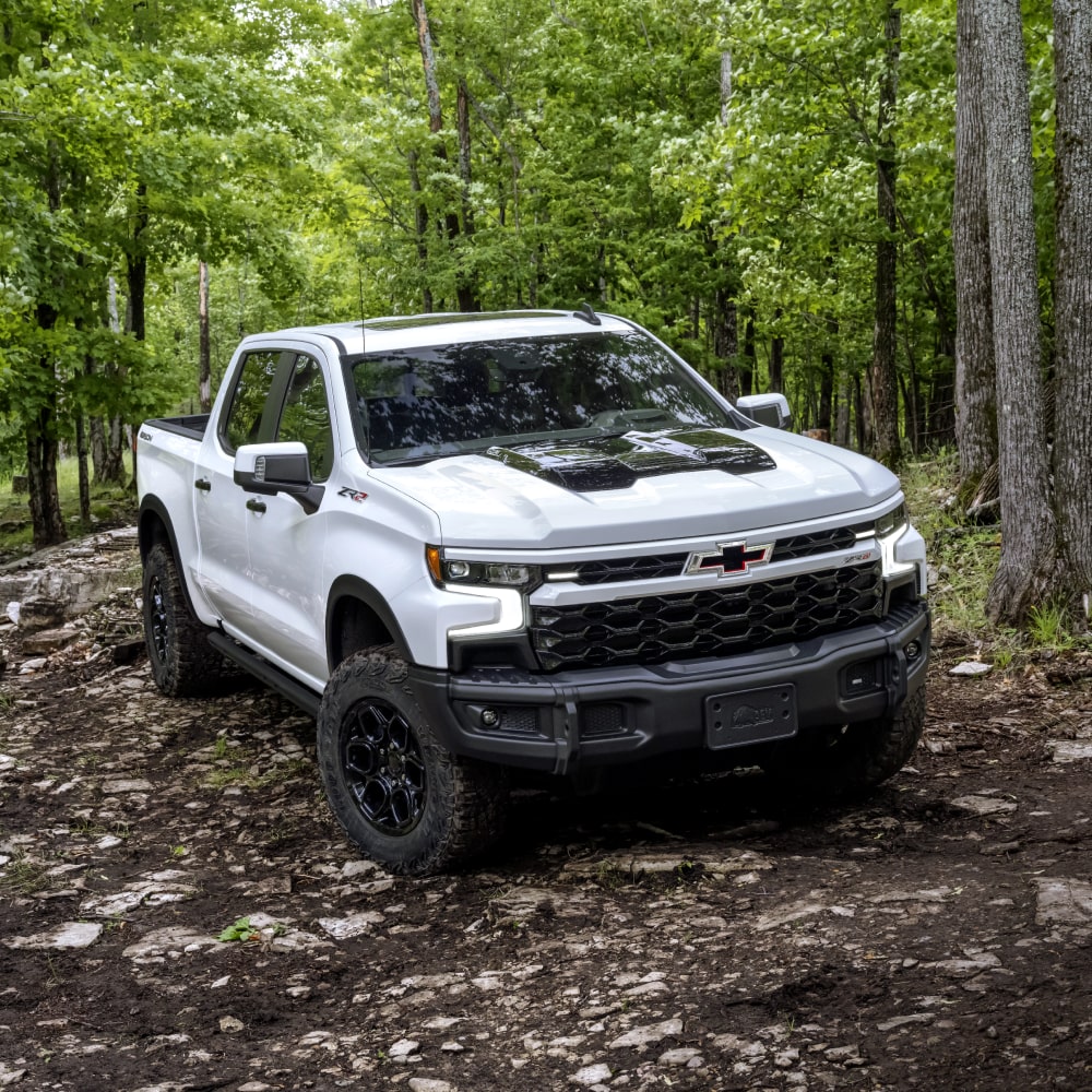 Vue en diagonale d’un Chevrolet Silverado LD 2025 blanc en conduite en forêt.