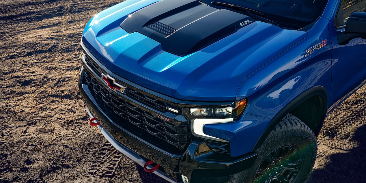 The polished ridged hood of the 2024 Chevrolet Silverado on a rocky terrain.