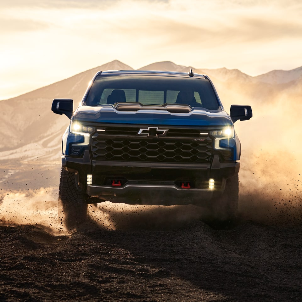 Vue avant d’un camion Chevrolet ZR2 en mouvement dans le désert au coucher du soleil.