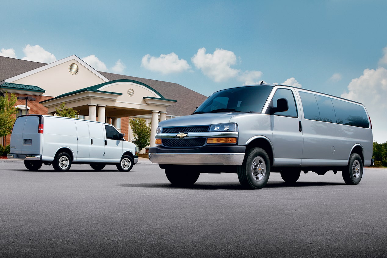 Two 2024 Chevrolet Express Vans parked parallel to each other outside a house.