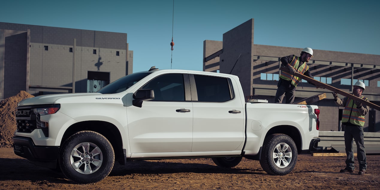 Two workers at a construction site unloading materials from a 2024 Chevrolet Silverado work truck.