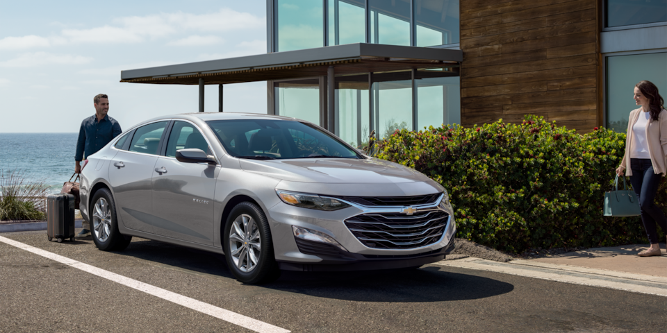 Un homme ouvre le coffre de sa Chevrolet Malibu 2024 dans le terrain de stationnement d’un hôtel.