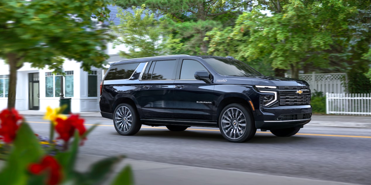 Front-side view of the 2025 Chevrolet Suburban SUV driving in the neighbourhood.