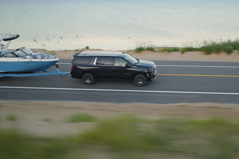 Side view of the 2025 Chevrolet Suburban towing a boat while driving down the road.