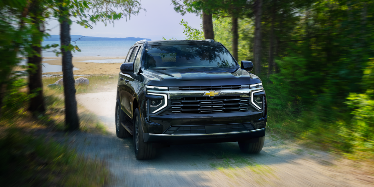 Vue avant du VUS Chevrolet Tahoe 2025 en mouvement sur un chemin de terre bordé d’arbres.