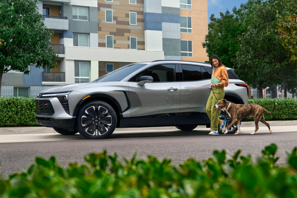 Vue latérale du Chevrolet Blazer EV 2025 avec une personne et un chien qui passent à côté.