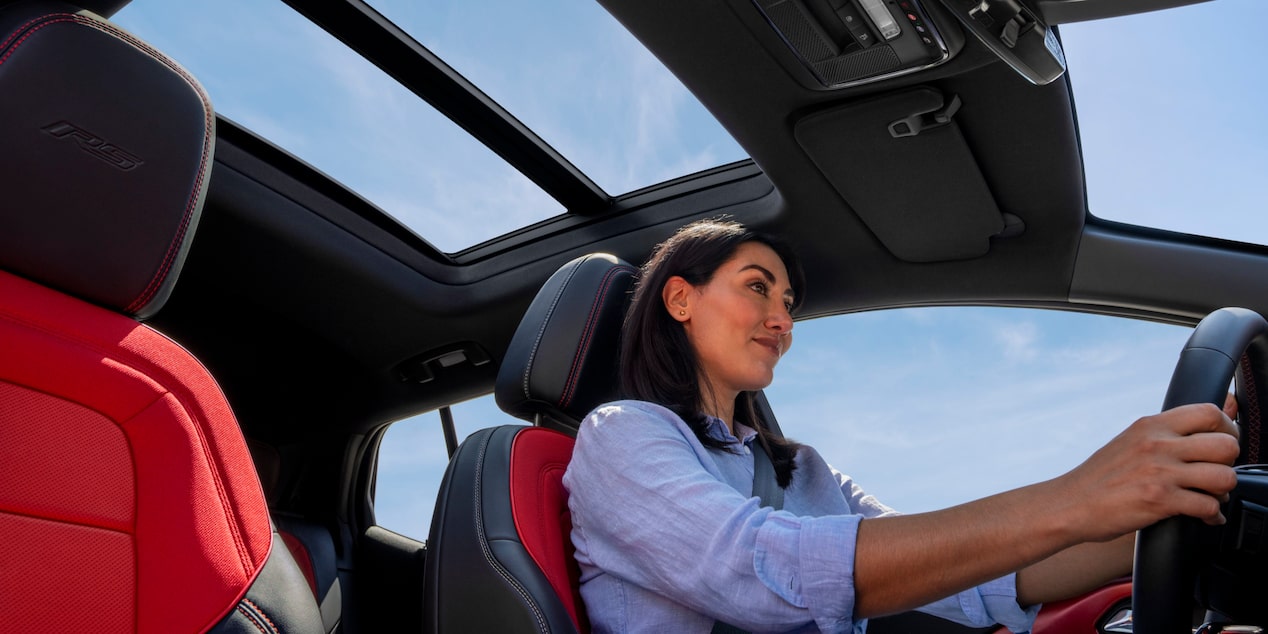 Vue latérale d’une personne au volant du Chevrolet Equinox EV 2025 sous un beau ciel bleu.