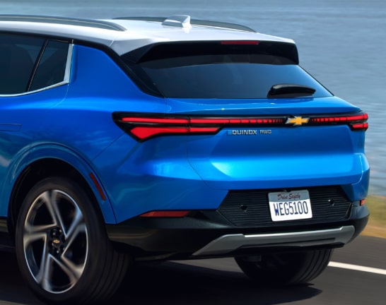 Three Quarters Rear View of a Blue 2025 Chevy Equinox EV Driving Down the Road