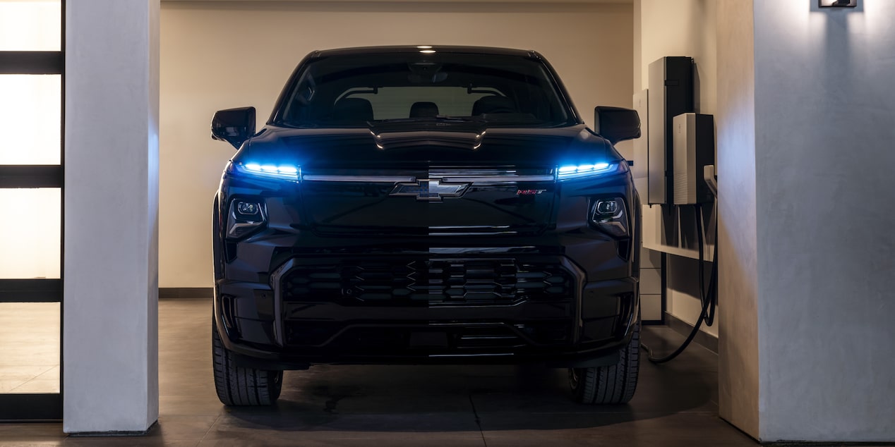 Front view of a 2025 Chevrolet Silverado EV charging in a home garage at night.