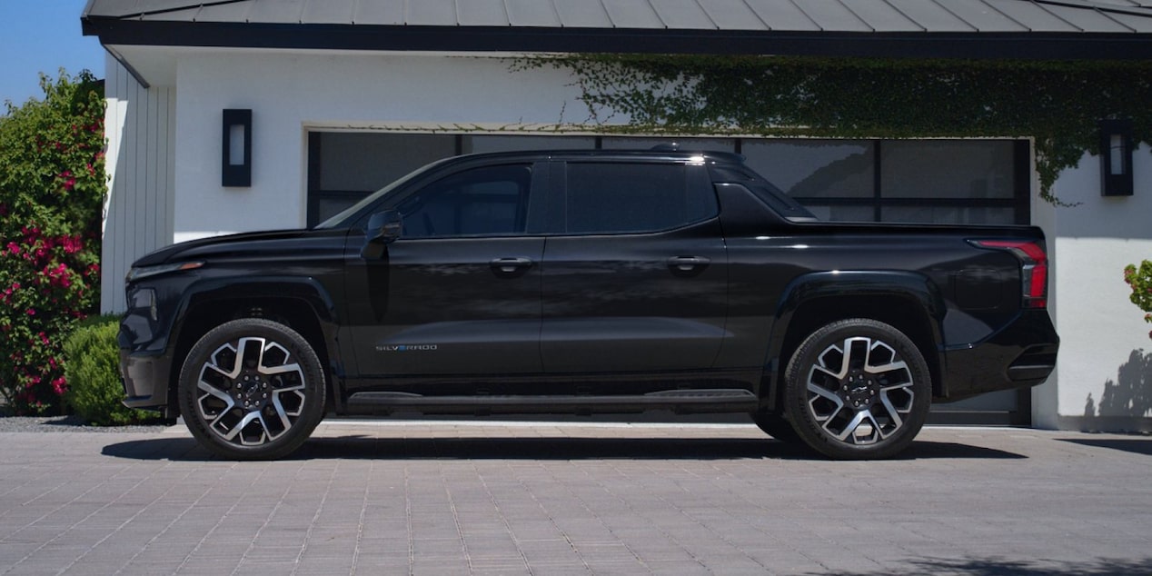 Side view of a 2025 Chevrolet Silverado EV parked next to a house surrounded by trees.