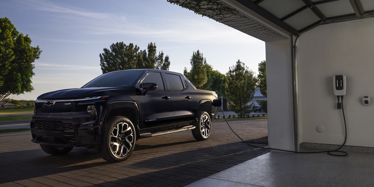 A 2025 Chevrolet Silverado EV next to a garage getting charged.