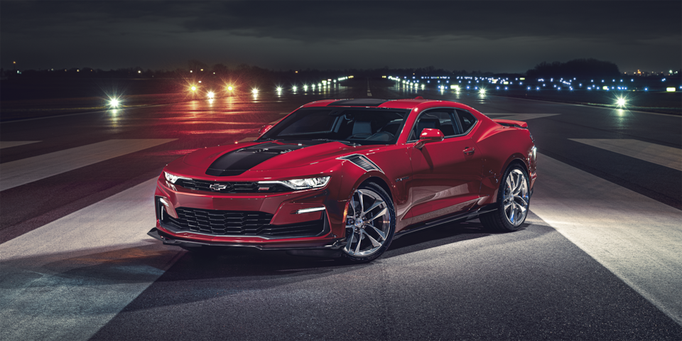 Red and black colored 2024 Chevrolet Camaro parked on an airplane tarmac at night.