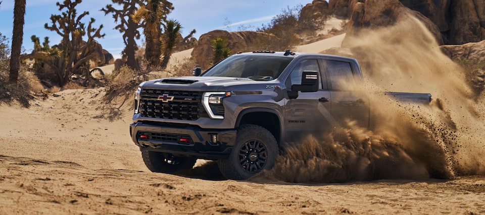 Front-side view of the 2025 Chevrolet Silverado HD pickup truck skidding in a sandy terrain.