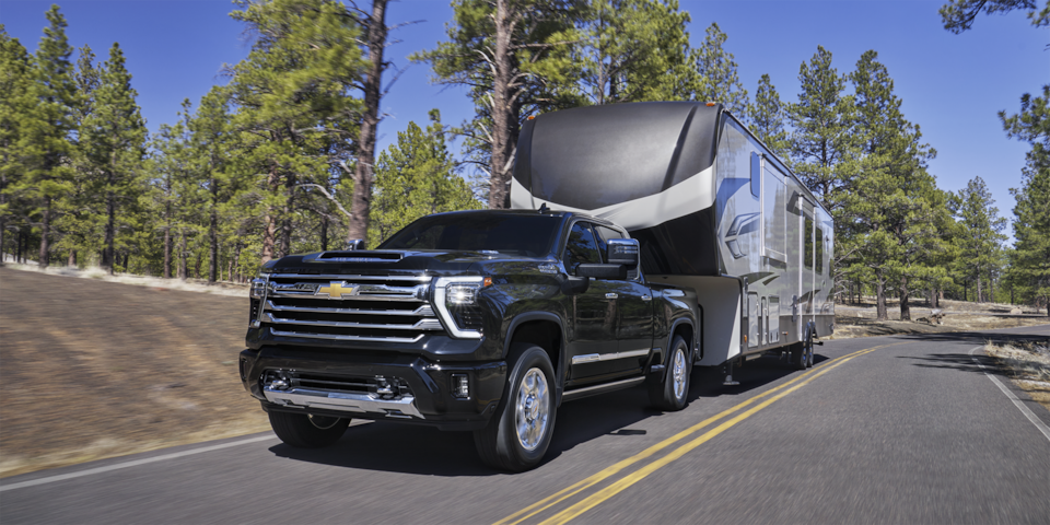 A 2025 Chevrolet Silverado HD pickup truck towing a trailer in a countryside road.