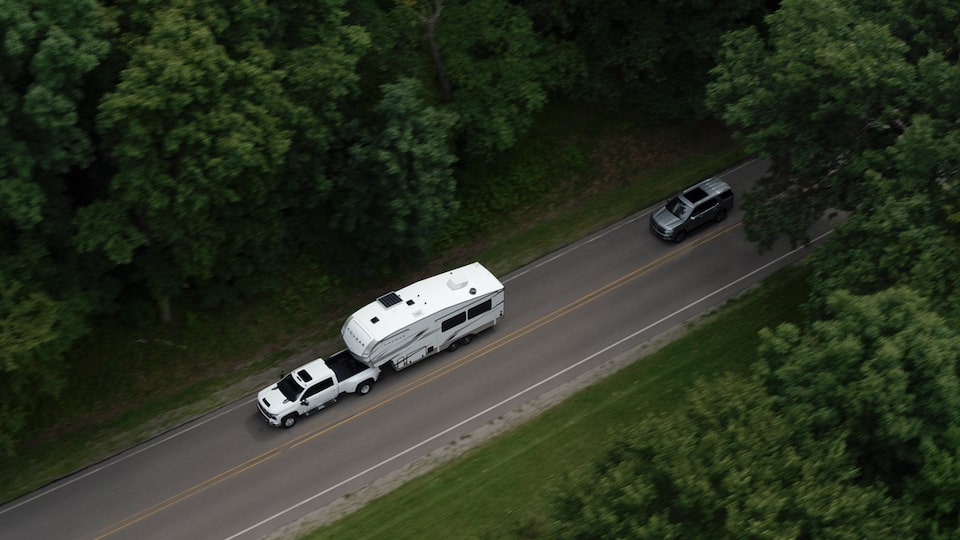 Bird's eye view of the 2025 Chevrolet Silverado HD pickup truck towing a trailer in a tree-lined road.