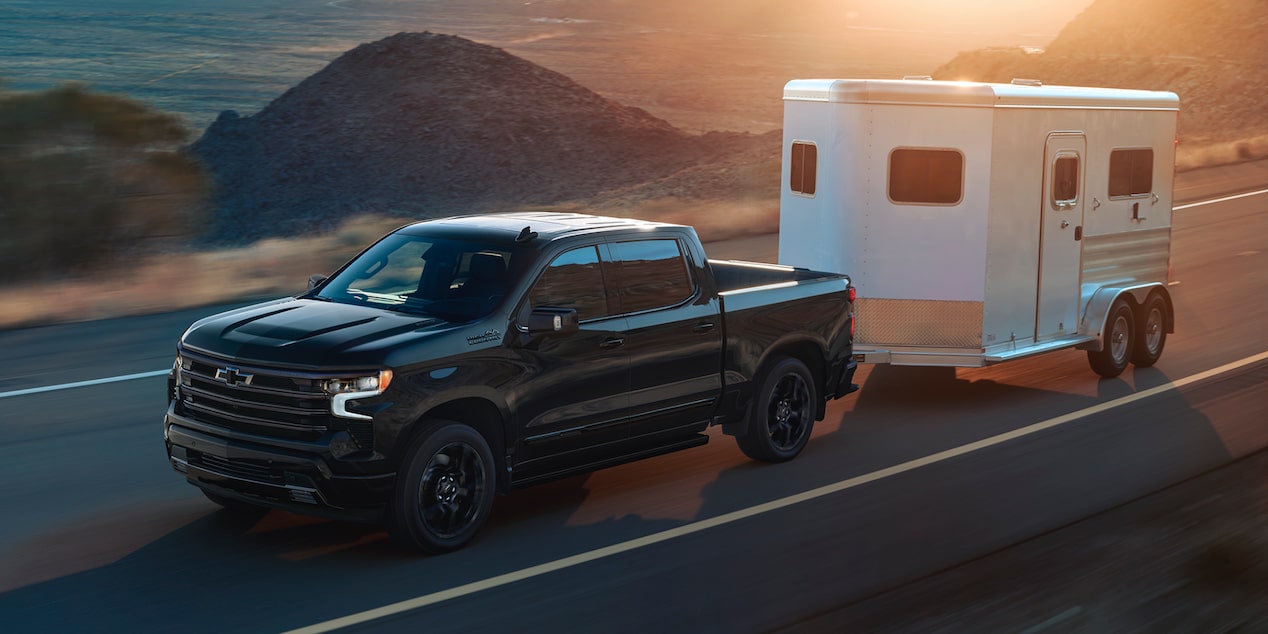 Un Chevrolet Silverado LD 2025 noir sur la route avec une remorque dans un paysage enneigé.