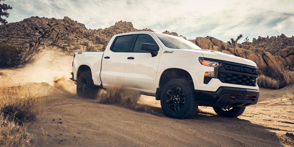 Three quarters view of a white 2025 Chevrolet Silverado LD driving on a desert plain.