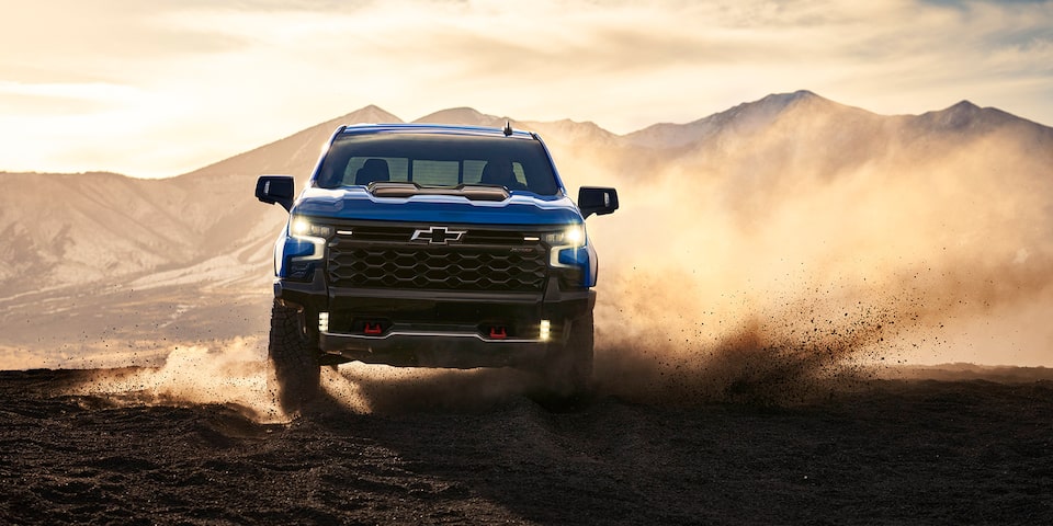 Vue avant du pick-up Chevrolet Silverado LD 2025 sur une route poussiéreuse, par une journée ensoleillée.