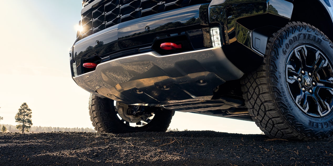 Front grille of a blue 2025 Chevrolet Silverado LD parked on a muddy terrain.