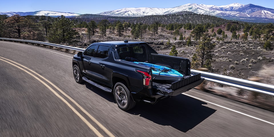 2024 Chevrolet Silverado EV driving on a highway with a kayak stowed in the bed.