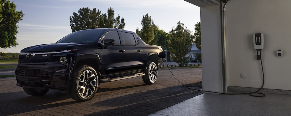 2024 Chevrolet Silverado EV parked outside a garage while plugged into a charging station.