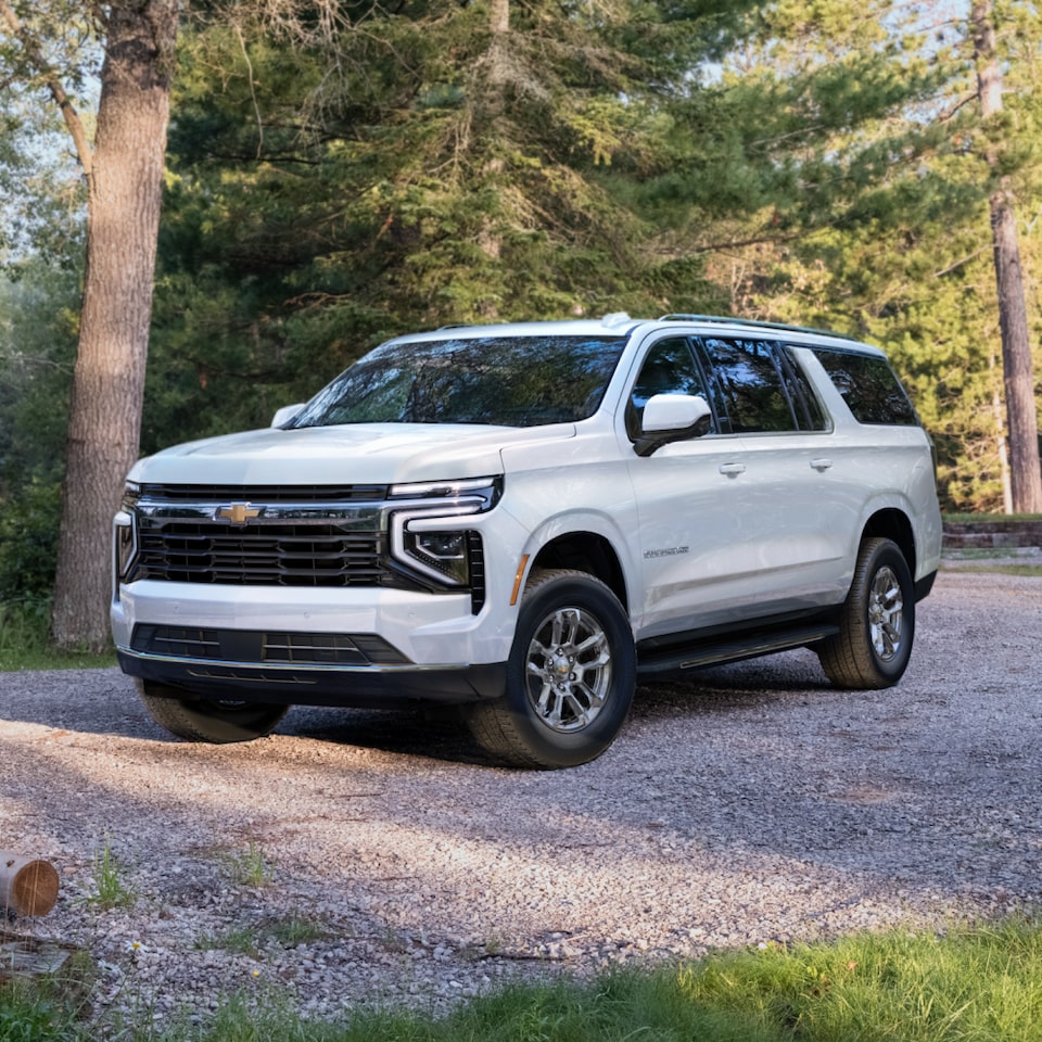 Front Three-Quarters View of the 2025 Chevrolet Suburban SUV Parked on a Gravel Road in a Forest