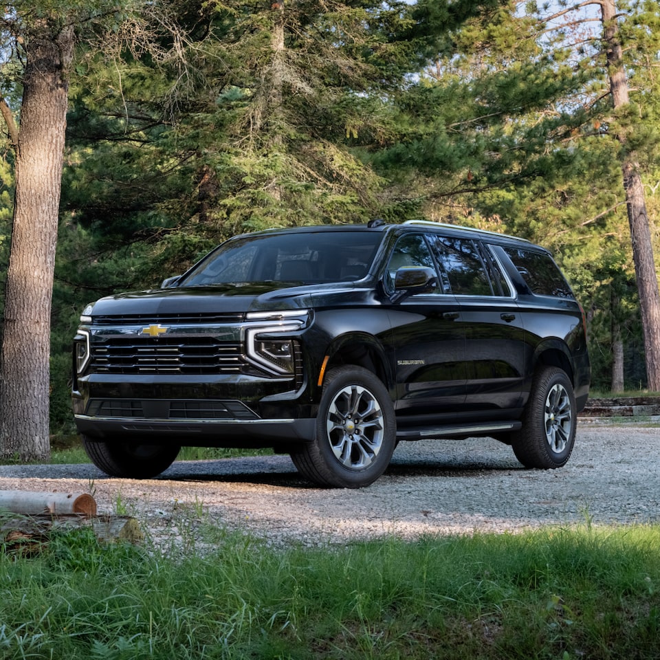 Front Three-Quarters View of the 2025 Chevrolet Suburban SUV Parked on a Gravel Road in a Forest