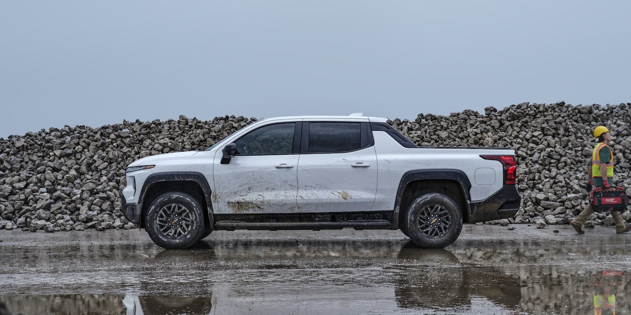 Side view of a white 2025 Chevrolet Silverado EV Work Truck parked on a wet plain.