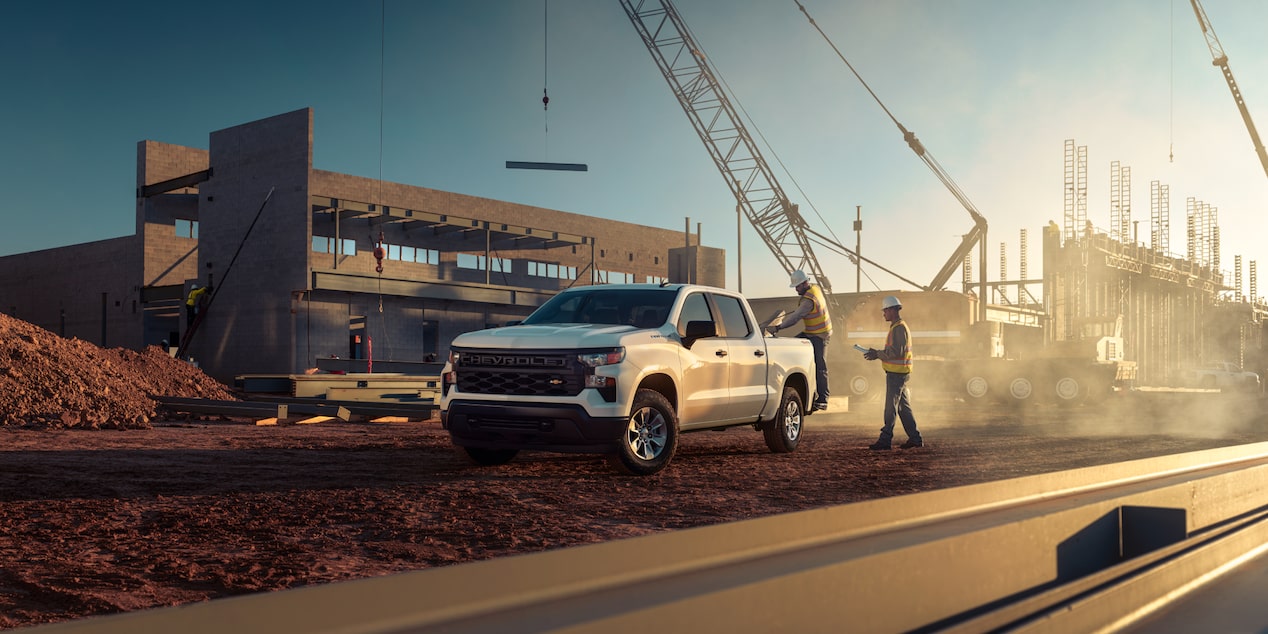 Two construction workers standing near a 2025 Chevrolet Silverado LD Work Truck.