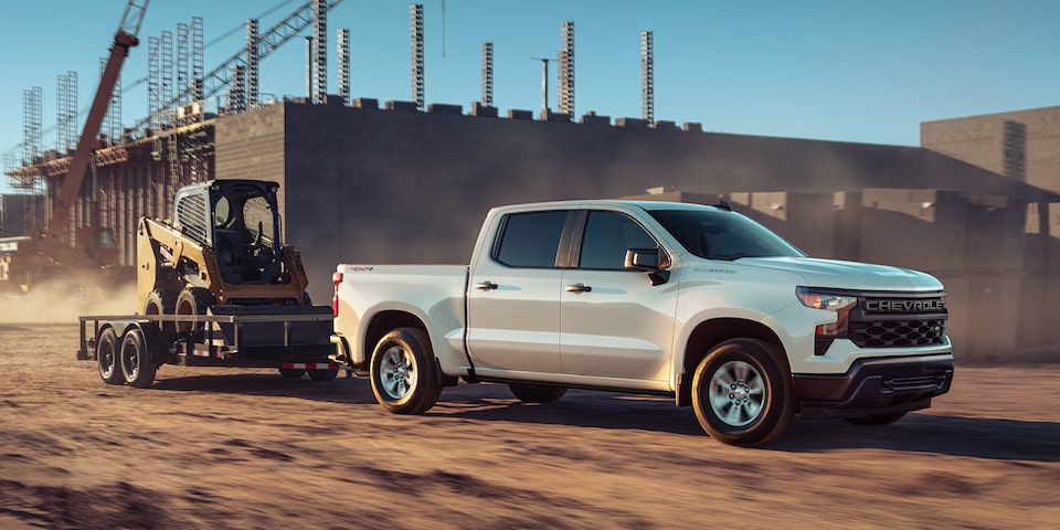 A 2025 Chevrolet Silverado LD Work Truck towing a skid loader on a trailer.